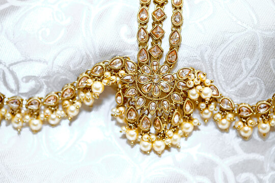 a closeup view of an elegant gold necklace with intricate design and pearls on a white background.