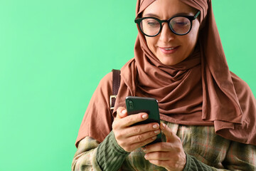 Mature Muslim woman using mobile phone on green background, closeup