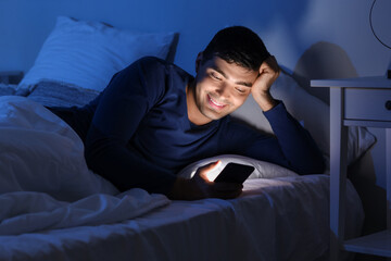 Fototapeta premium Young man using mobile phone in bed at night