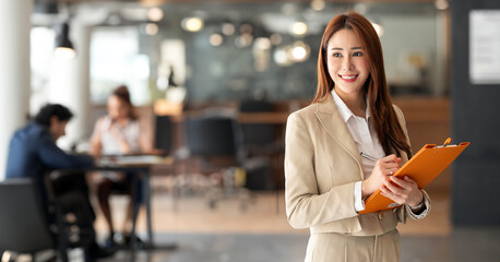 Smiling confident business leader holding file folder, looking at camera and standing in an office...