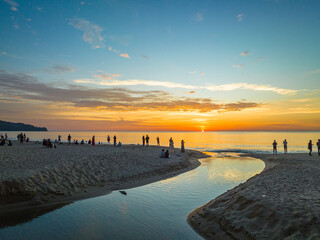 .aerial view of the winding canal on the sandy beach..Tourists watch the sun set beside a small...