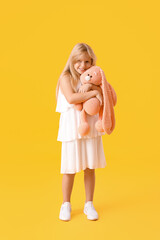 Cute little girl with plush bunny toy on yellow background