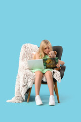 Cute little girl with teddy bear reading fairy tale book while sitting on armchair against blue...