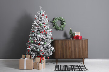 Decorated Christmas tree with gifts and dresser against grey wall