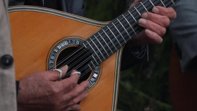 Strumming a Portuguese guitar outdoors. Close up
