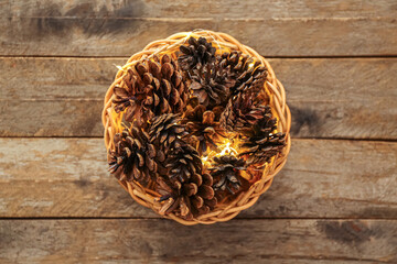 Fototapeta na wymiar Wicker bowl with pine cones and Christmas glowing lights on wooden background