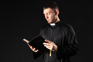 Young priest reading Holy Bible on black background