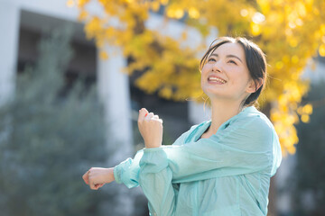 紅葉の中運動をする若い女性の秋冬のイメージ　準備運動のストレッチのクローズアップ　左にコピースペースあり