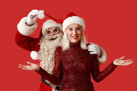 Santa Claus with beautiful mature woman in Christmas glasses and hats on red background - Powered by Adobe