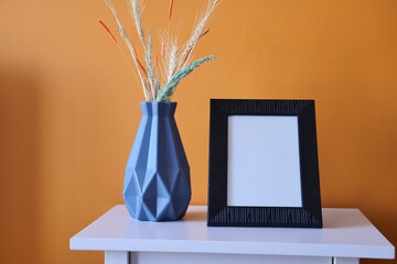 Black frame mockup on table against orange color wall,