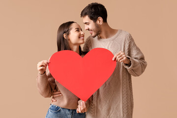 Beautiful young couple with red paper heart on brown background. Valentine's day celebration
