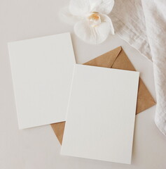 Greeting Cards mockup, empty white blanks, envelopes and orchid flower  top view on beige...