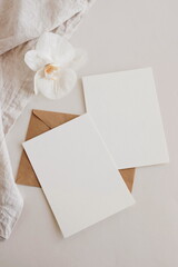 Greeting Cards mockup, empty white blanks, envelopes and orchid flower  top view on beige background with copy space. flat lay. Empty white  Blank, greeting card template, invitation.