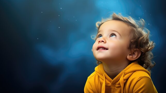 A surprised little boy 3-4 years old looks up on a blue-yellow background. space for text