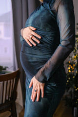 Female hands touching her belly. She is pregnant. Girl is dressed in a blue elegant dress. Her...