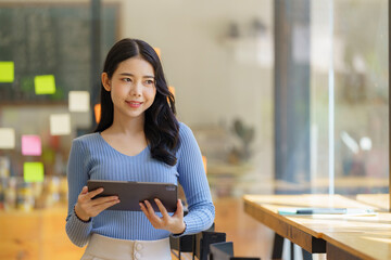 A beautiful Asian businesswoman holding a digital tablet while standing in the office room....