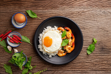 Stir-fried shrimp with basil Thai street food arranged on a black plate with a fried egg Spicy Thai food placed on a wooden table. Top view.