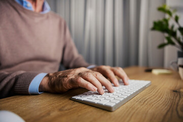 Close up of older executive hands typing on keyboard at home office.