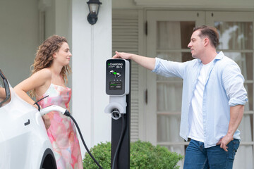 Happy and lovely couple with eco-friendly conscious recharging electric vehicle from EV home...