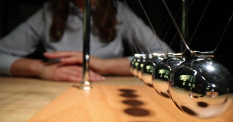 Woman investor sits at table playing with tabletop pendulum with Newton cradle in modern office