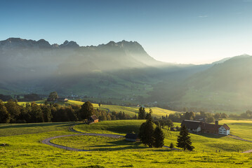 Rural landscape in the Appenzell region with farm houses and meadows in the last light of the evening sun, view to the Alpstein mountains with Saentis, Canton of Appenzell Innerrhoden, Switzerland