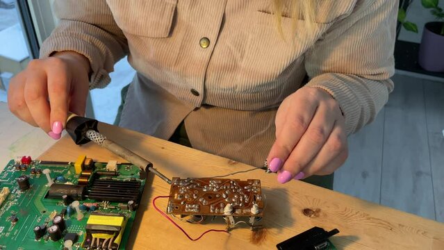 Close up woman hands Soldering a micro chip processor with iron tool on a green circuit boad. Electroncs service technology and macro computer concept background.