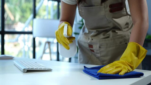 The young housekeeper wore gloves and cleaned the work table with a rag and cleaning spray. Professional office home cleaning products Providing hygiene services Free from germs.