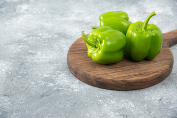 Fresh green bell peppers placed on a wooden round board