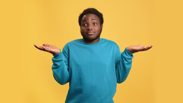 Doubtful African young man shrugging don't know not sure uncertain gesture posing isolated on orange