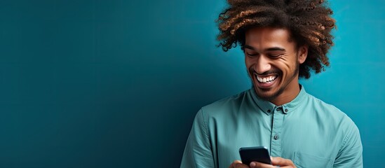 Smiling young man in casual clothes leaning on a blue wall, looking at a cellphone in Quebec City, Canada. - Powered by Adobe