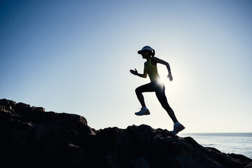  Woman runner running on sunrise seaside rocky mountains