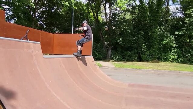 Ein Mann, der mit Inlineskates auf einer Halfpipe in einem Skatepark f&auml;hrt. Der Mann tr&auml;gt einen Helm und f&uuml;hrt einen Trick aus. Die Rampe ist aus Holz und gebogen.