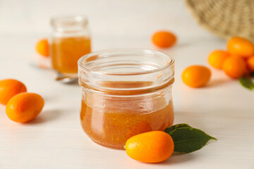Kumkvat and jars of jam on light background, close up