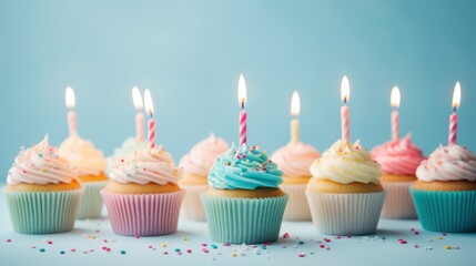 Birthday cupcakes with colorful candles on a pastel blue background.