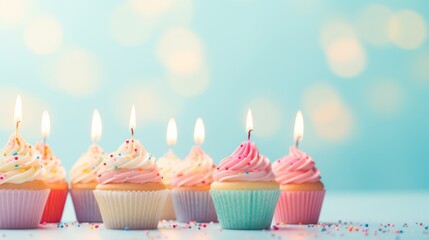Birthday cupcakes with colorful candles on a pastel blue background.