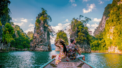 a couple traveling by longtail boat exploring epic limestone cliffs in a huge lake in Khao Sok National Park, Chiew Lan Lake, Thailand Surat Thani, men and woman in front of longtail boat - obrazy, fototapety, plakaty