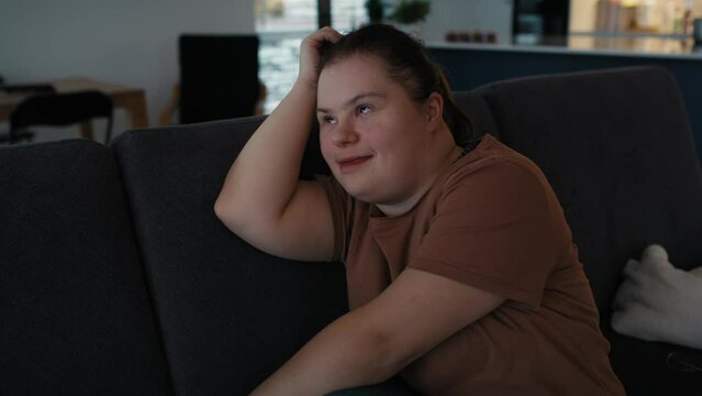 Thoughtful down syndrome woman sitting on sofa and looking away. Shot with RED helium camera in 8K.     