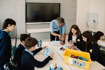 Kids and teacher using constructor blocks and tablet while studying robotics in stem education class