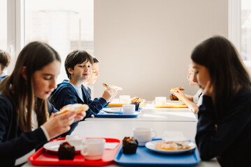 Group of school children having lunch while sitting in school cafeteria - Powered by Adobe