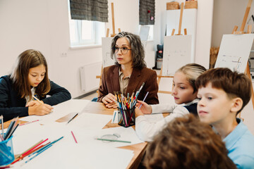 Teacher giving school kids drawing lesson in art school