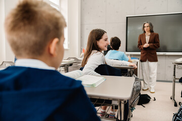 Portrait of school girl turning back and talking to classmate while sitting in classroom
