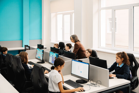 Teacher helping school kids using personal computers during computer science class