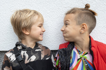 Two brothers or friends 7 years old, facing each other on a white background, make funny faces and...
