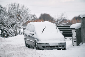 A car parked outdoors in winter is covered with snow and ice. The wiper blades are lifted up to...