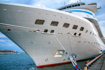 Naklejka premium A large white cruise ship is moored in the port. Cruise ship bow. Ropes hold the ship on the dock. Ship cables