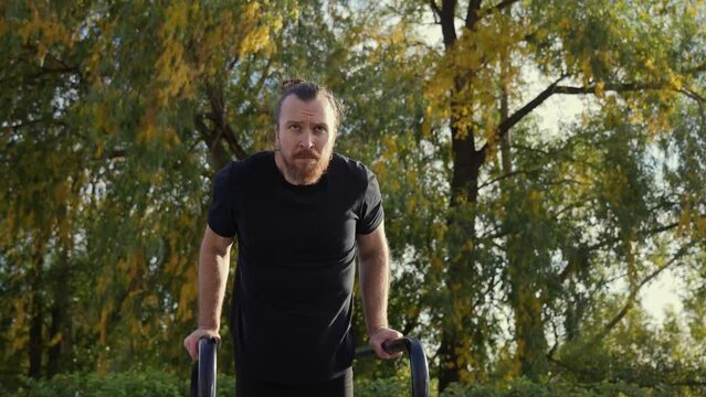 Caucasian man doing parallel bars exercises outdoors in autumn. Slow motion. 