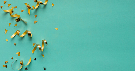 close up on group of gold color of rolling ribbon and confetti on teal background with copy space...