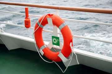 An orange lifebuoy on the ship hangs on the railing of the side. A lifebuoy on a passenger liner