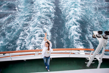 A girl poses on the stern of a cruise ship while traveling on the ocean. Luxury vacation on a sea...