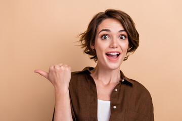 Photo of adorable excited lady wear brown shirt pointing thumb empty space isolated beige color background